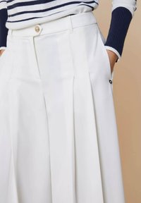 Witte plissé broek met een soepele structuur, voorzien van een knoopsluiting en zijzakken, aangevuld met mouwen met marineblauwe strepen.