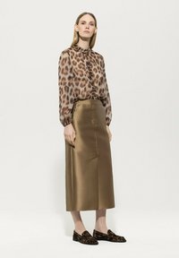 Bluse mit Leopardenmuster und Rüschensaum, satinierter bronzefarbener Rock und schwarze Slipper mit Leopardenakzenten. Glatte Texturen und taillierte Passform.
