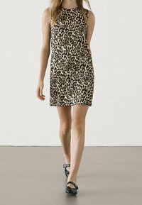 Hihaton leopardi kuvioinen mekko beigestä ja mustasta, polvimittainen. Sileä pinta ja pyöreä pääntie; yhdistetty mustiin tasapohjaisiin kenkiin.