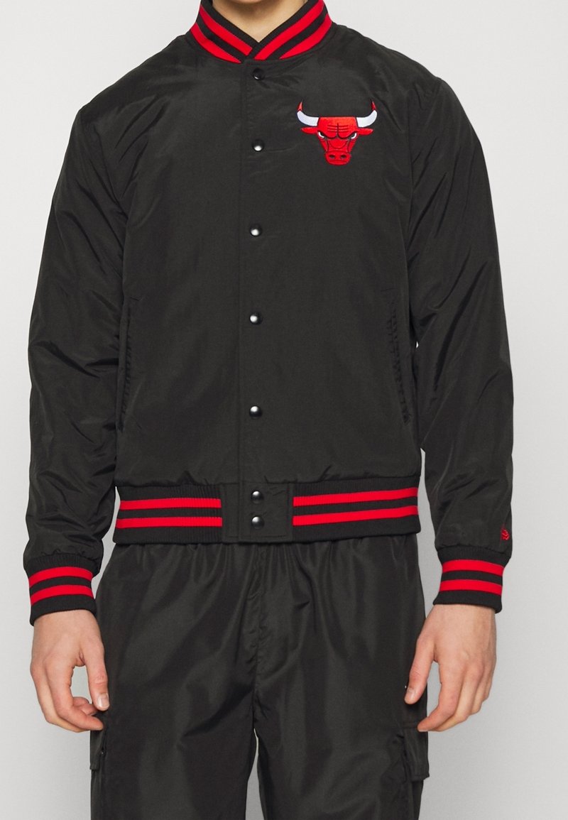 Svart bomberjacka med randiga ribbade kragar och resårmanchetter i rött och svart. Har en broderad röd tjurlogotyp på vänster bröst.