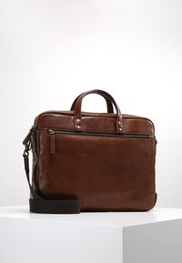 Sac en cuir marron avec une texture lisse, double poignée supérieure, une bandoulière amovible, et une poche zippée sur le devant. Design minimaliste.