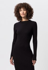 Abito nero a maniche lunghe, aderente, in maglia a coste, con scollo rotondo e spacchi sui lati dell'orlo. Il tessuto sembra testurizzato e elasticizzato.