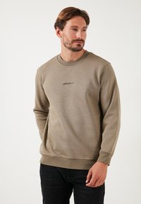 Sudadera color caqui en una suave mezcla de algodón, con cuello redondo, mangas largas, puños acanalados y un pequeño logo negro en el pecho.