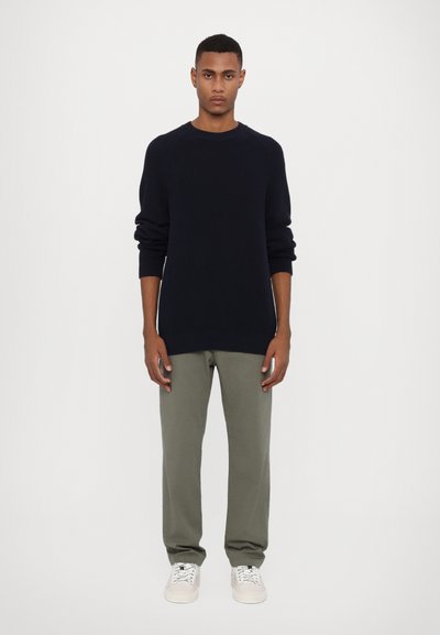 Pull en maille navy avec un motif texturé, col rond et manches côtelées, associé à un pantalon olive et des baskets blanches.