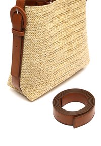 Vävd kransväska med ljusbeige utsida, bruna läderdetaljer och en avtagbar brun läderrem som ligger ihopvriden bredvid.