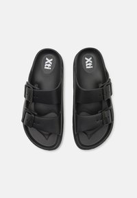 Sandale negre cu talpă plată, dotate cu două catarame ajustabile; realizate dintr-un material plastic neted; cu o talpă conturată pentru confort; design minimalist.