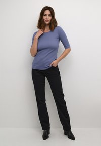 Ljuslila, åtsittande t-shirt med trekvartsärmar, som parats ihop med svarta raka byxor och svarta spetsiga stövlar.