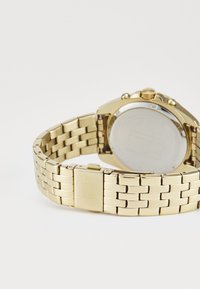 Orologio da polso in oro con bracciale a maglia metallica, dotato di cassa rotonda e un fondello riflettente in argento. Dettagli sulla corona e sulla chiusura.