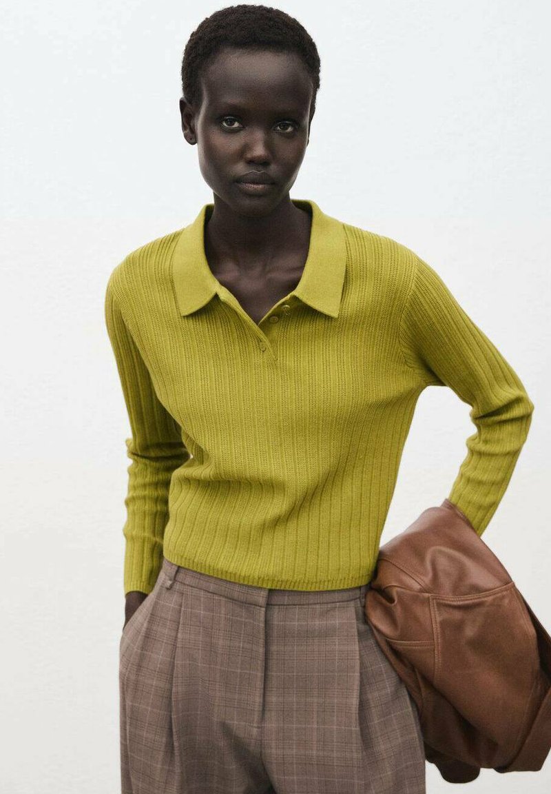 Camicia a maniche lunghe verde oliva a coste con colletto, abbinata a pantaloni a quadri a vita alta e una borsa a tracolla in pelle marrone.
