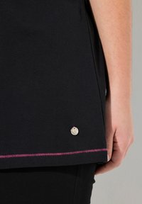 Camiseta negra hecha de tela suave, con un dobladillo curvado, costura rosa en la parte inferior y un acento decorativo plateado.