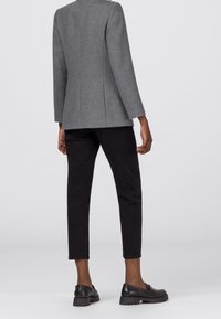 Šedé na míru ušité sako s výrazným střihem, kombinované s černými zúženými kalhotami a černými mokasíny. Hladká látka s minimem detailů.