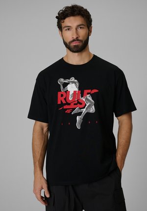 Hombre con barba que lleva una camiseta negra con un gráfico de jugador de baloncesto y texto rojo "RULES" sobre un fondo gris liso.