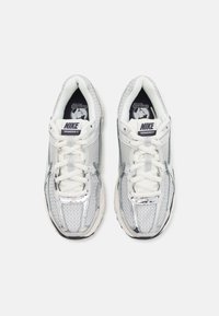Paire de chaussures de course Nike Vomero 5 blanches et argentées vues de dessus sur fond blanc.