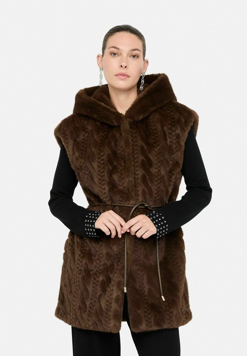 Gilet in finta pelliccia marrone con un design a maglia a treccia testurizzata, cappuccio e vita cintrata. Maniche lunghe nere con polsini borchiati.