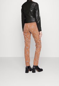 Chaqueta de cuero negra con hombros texturizados y diseño ajustado, combinada con pantalones naranja con estampado y botas negras de tacón grueso.