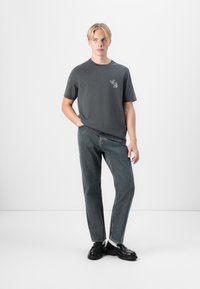 Gray cotton t-shirt with a small graphic on the left chest, paired with straight-leg blue jeans and black leather shoes.