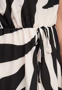 Čierno-biele zebra pruhované tkaniny, so elastickým pásom a viazacími detailmi. Materiál vyzerá ľahko a štruktúrovane.