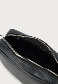 Černá kožená taštička s texturovaným povrchem a stříbrným zipem. Uvnitř se nachází černá látková podšívka a malá štítková značka.