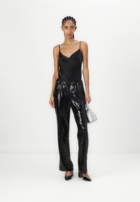 Svart sateng camisole topp med tynne stropper, kombinert med glitrende bukser med svarte paljetter. Modellen holder en liten sølvfarget håndveske og har på seg svarte høyhælte sko.