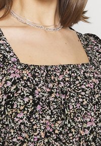 Svart blommig topp med samlad halsringning, prydd med små rosa och gröna blommor. Mjuk kvalitet med fyrkantig halsringning och puffärmar.