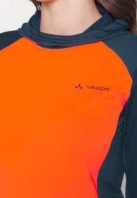 Långärmad tröja med huva, med en livlig orange framsida och mörkblå ärmar. Tyget verkar lätt och har en slät textur.