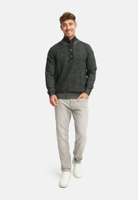 Strikket mørkegrå sweater med kvart-zip krave, to knapper og ribbede manchetter, parret med lysegrå bukser og hvide sneakers.