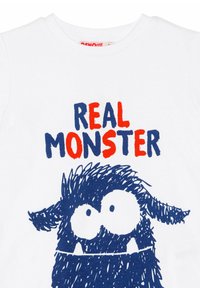 Weißes Baumwoll-T-Shirt mit einem blauen Cartoon-Monster-Design, das zwei auffällige Augen zeigt, und dem Text "REAL MONSTER" in Rot und Blau.