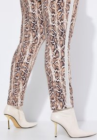 Strakzittende broek met een slangprint in beige en bruin, met witte zijstrepen. Gepaard met crèmekleurige stiletto enkellaarzen.