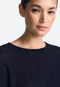 Granatowy sweter dzianinowy z teksturowanym wzorem, z szerokim dekoltem i prążkowanymi wykończeniami na krawędziach. Miękki, lekki materiał.