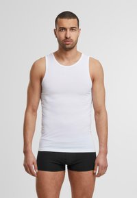 Top de algodón blanco sin mangas con tirantes amplios, diseño ajustado. Combinado con pantalones cortos negros de boxeador, textura lisa, mínima marca.