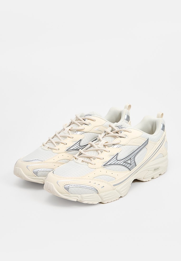 Zapatillas deportivas beige con parte superior de malla, detalles plateados, suela texturizada y un sistema de cordones prominente. Punta redondeada y diseño de cuello acolchado.