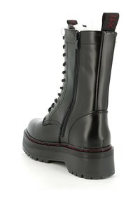 Stivale da combattimento in pelle verniciata nera con suola spessa, zip laterale, lacci frontali e dettagli in contrasto con cuciture rosse.