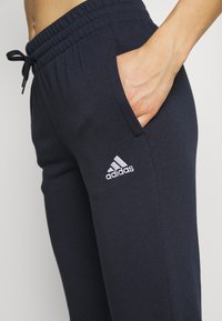 Pantalones deportivos de color navy con cintura ajustable, bolsillos laterales y un logo blanco de Adidas en la pierna izquierda. Tejido suave y elástico.