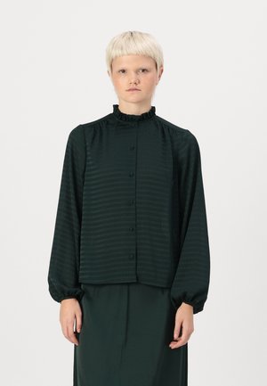 Mörkgrön blus med en volangkrage, knappfront och långa ärmar. Har en subtil vertikal randig textur. Slätt tyg.