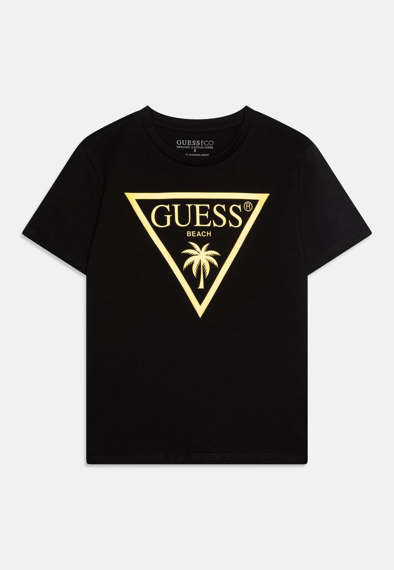 T-shirt en coton noir avec un logo triangulaire jaune portant le texte "GUESS BEACH" et un design de palmier au centre. Manches courtes, col rond.