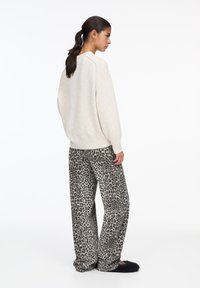 Pull en tricot beige avec des manches longues et un ourlet côtelé, associé à un pantalon à jambes larges en tartan noir et gris à imprimé léopard. Texture douce.