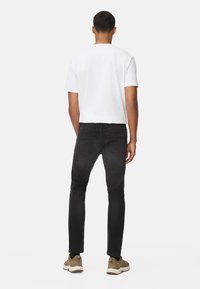 Schwarze Jeans und ein weißes T-Shirt. Die Jeans haben eine schmale Passform und Rückentaschen. Die Schuhe sind olivgrün mit weißen Sohlen.