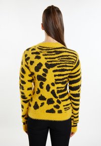 Geel sweater van zacht materiaal, met een zwart dierenmotief dat strepen en vlekken op de rug en mouwen heeft.