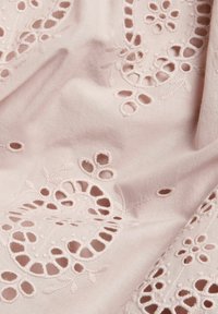 Ljust rosa tyg med intrikata blomsterbroderier och utklippta detaljer. Slät textur med synliga stygn och mönster.