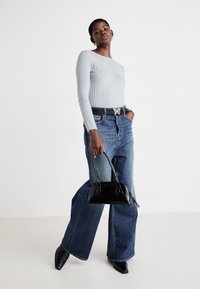Grå, ripete langermet topp, høyt liv blå flare-jeans, svart håndveske og spisse svarte hæler. Belte med sommerfuglspenne-detalj.