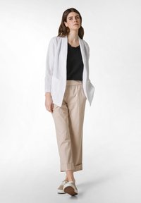 Valkoinen pellavapukujakku mustan paidan päällä, yhdistettynä beigeihin elastisiin housuihin ja vaaleanruskeisiin lenkkareihin. Mukana etutaskut ja käännetyt hihansuut.