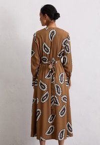 Braunes Midi-Kleid mit schwarz-weißen abstrakten Blattformen. Lange Ärmel und ein Taillenband, gefertigt aus einem glatten Stoff mit weicher Textur.