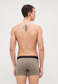 Boxershorts in einem grau-schwarz gestreiften Muster. Mit einem schwarzen elastischen Bund. Das Model hat ein Tattoo auf dem Rücken und steht mit dem Rücken zur Kamera.