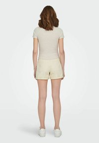 Lys grå ribbestrikket kortermet topp med en cropped passform, kombinert med kremfargede shorts, som har baklommer og oppbrettede ermer, iført hvite sneakers.