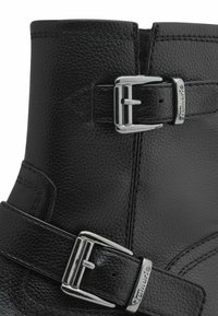 Bottine en cuir noir avec une finition texturée, accents de double boucle en argent et détails cousus sur la tige et les sangles.