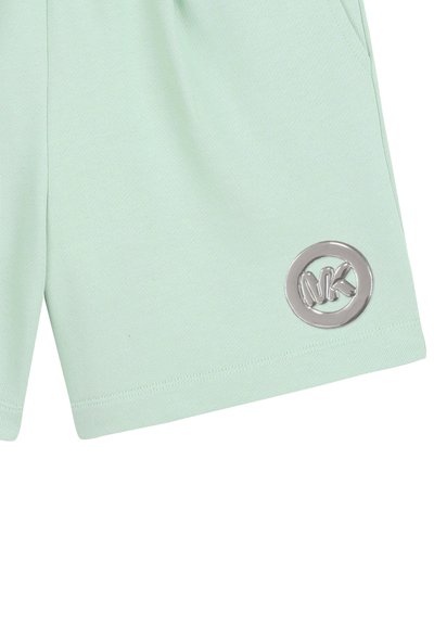 Shorts vert menthe clair avec un patch logo circulaire argenté près de l'ourlet sur la jambe gauche, légèrement pliés avec des coutures visibles et une poche latérale.