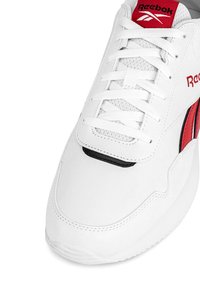 Fehér Reebok sportcipő piros kiegészítőkkel, fehér fűzőkkel, és logóval a nyelvén és oldalán, elölről és a felső oldal részleteit mutatva.
