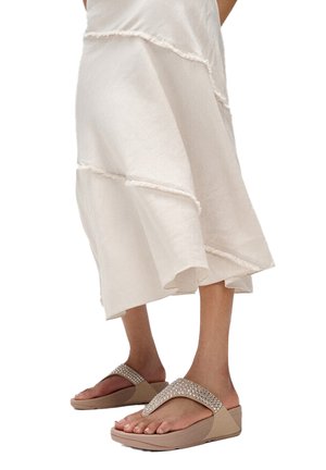 Tankleurige platform flipflops met een bandje versierd met strass-steentjes, gecombineerd met een vloeiende crèmekleurige rok met subtiele gelaagde naden.