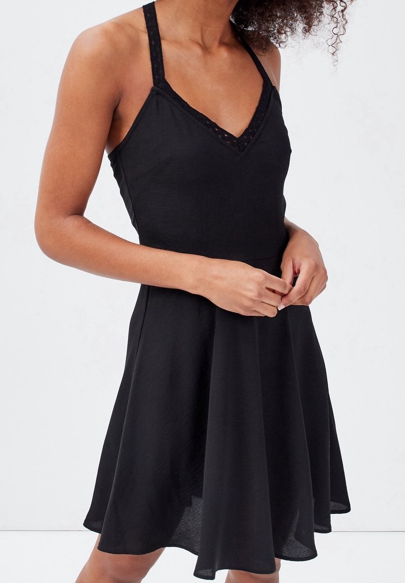 Schwarzes ärmelloses Kleid mit V-Ausschnitt, Spitze an den Trägern und einem ausgestellt Rock. Leichter Stoff mit glatter Textur.
