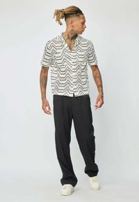 Chemise à manches courtes avec un motif zigzag noir et blanc, assortie à un pantalon noir et des baskets blanches. Tissu doux, coupe décontractée.